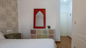 A bedroom with a bed, a dresser with patterned tiles, a mirror with an ornate frame, and a small elephant figurine. - Peñon Blanco       . (Níjar)