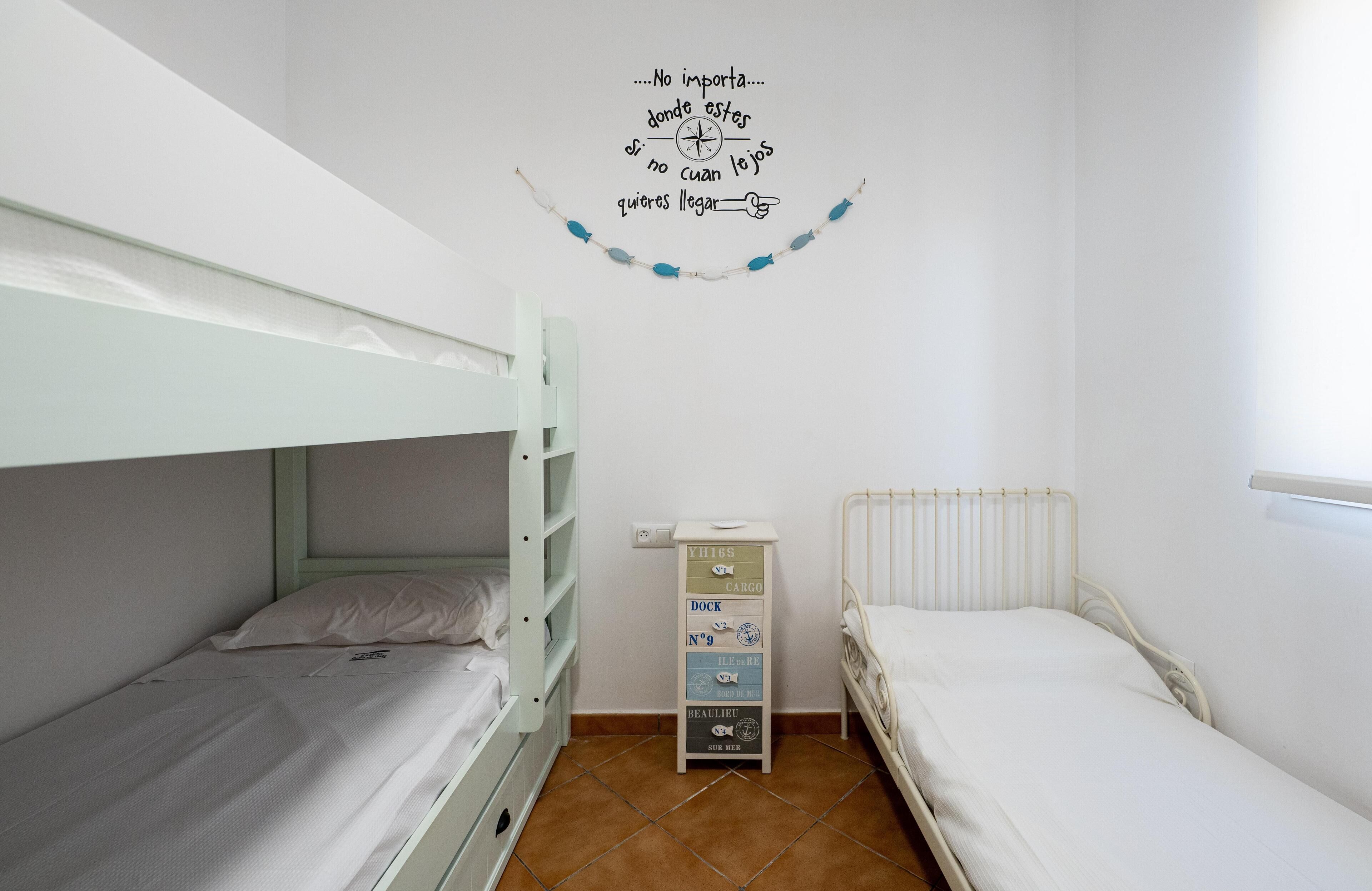 A bedroom with bunk beds, a small cabinet, and a wall decoration.