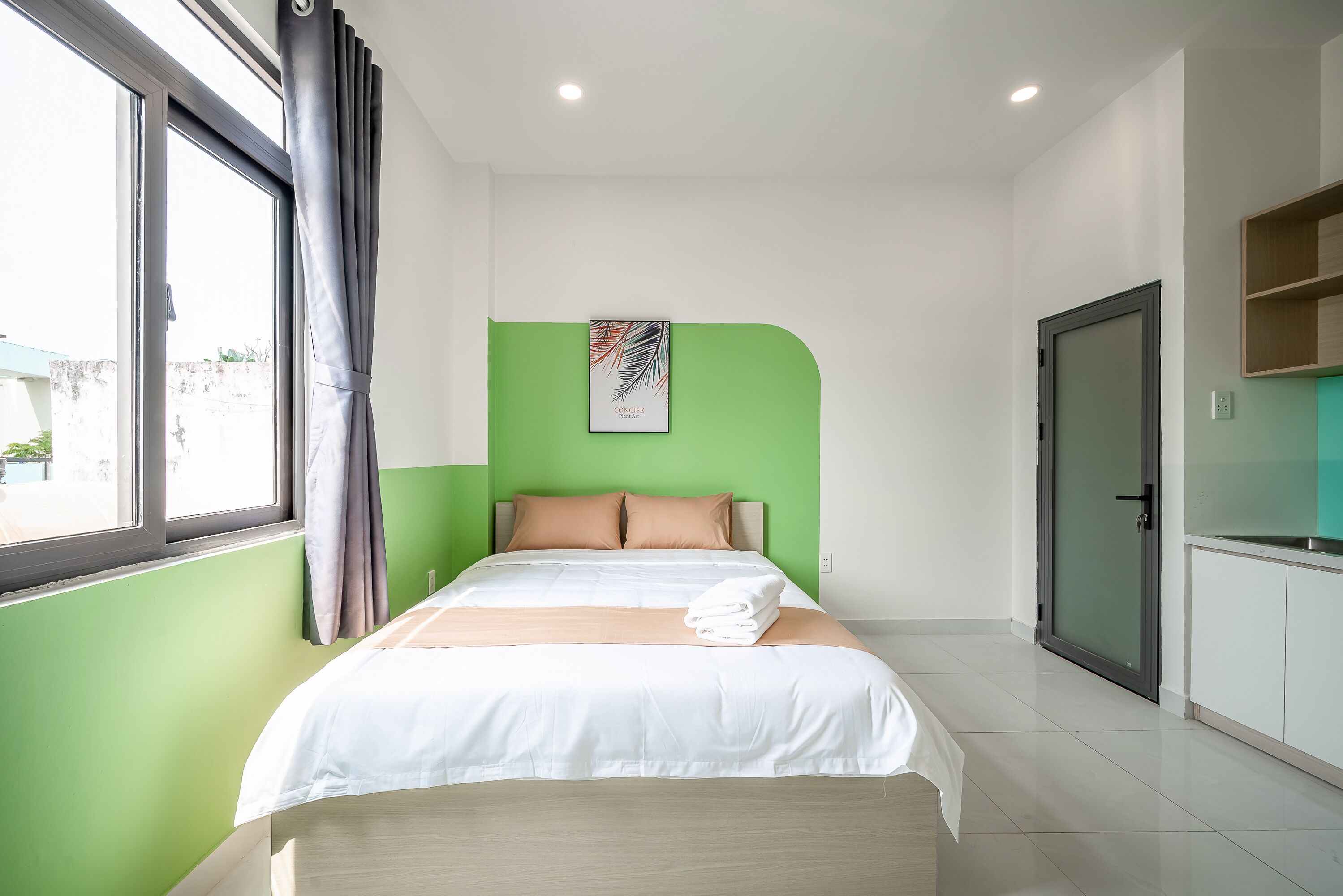 A neatly made bed with white linens, a green accent wall, and a framed artwork above it.