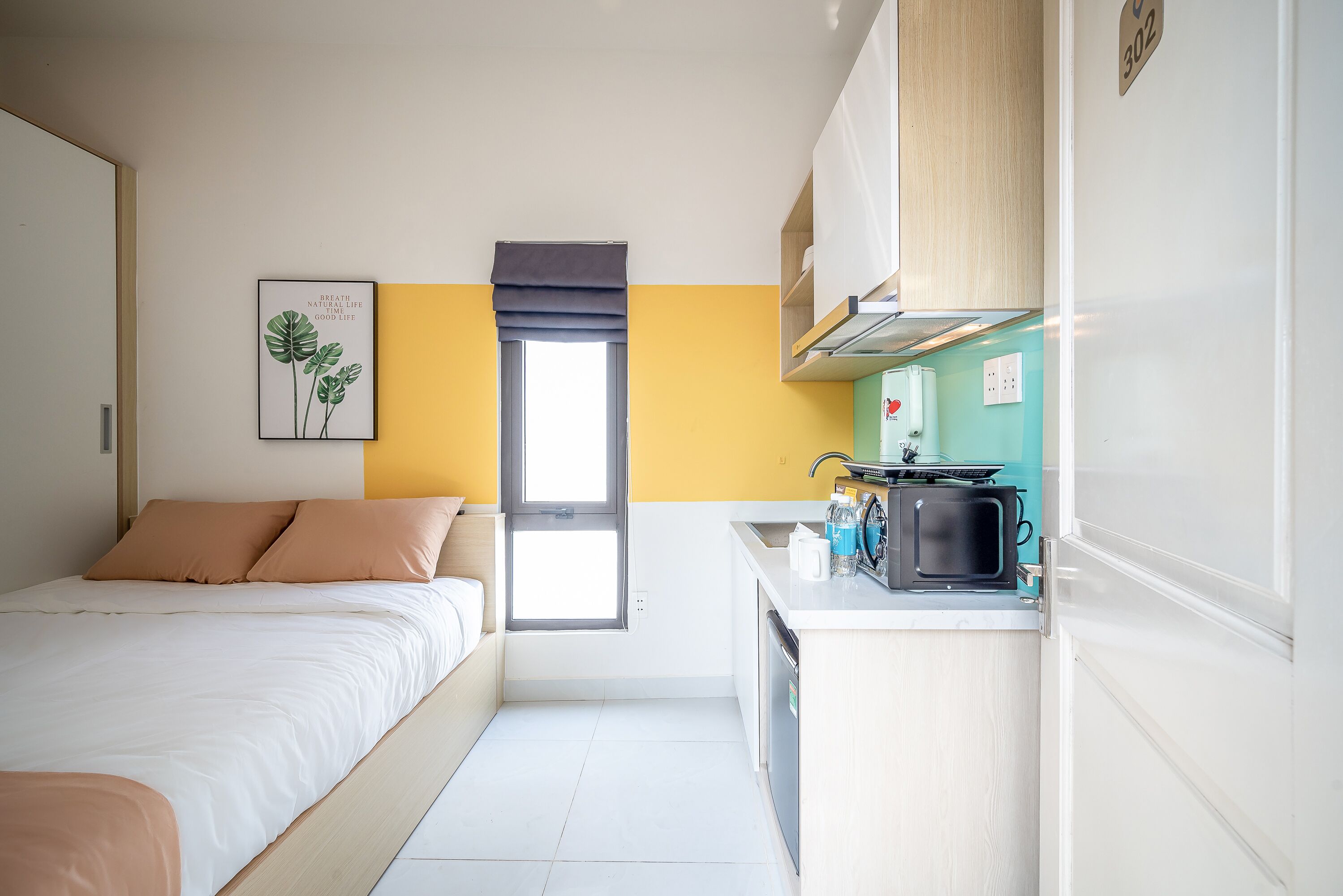 A bedroom with a bed, a window, and a kitchenette with a microwave and coffee maker.