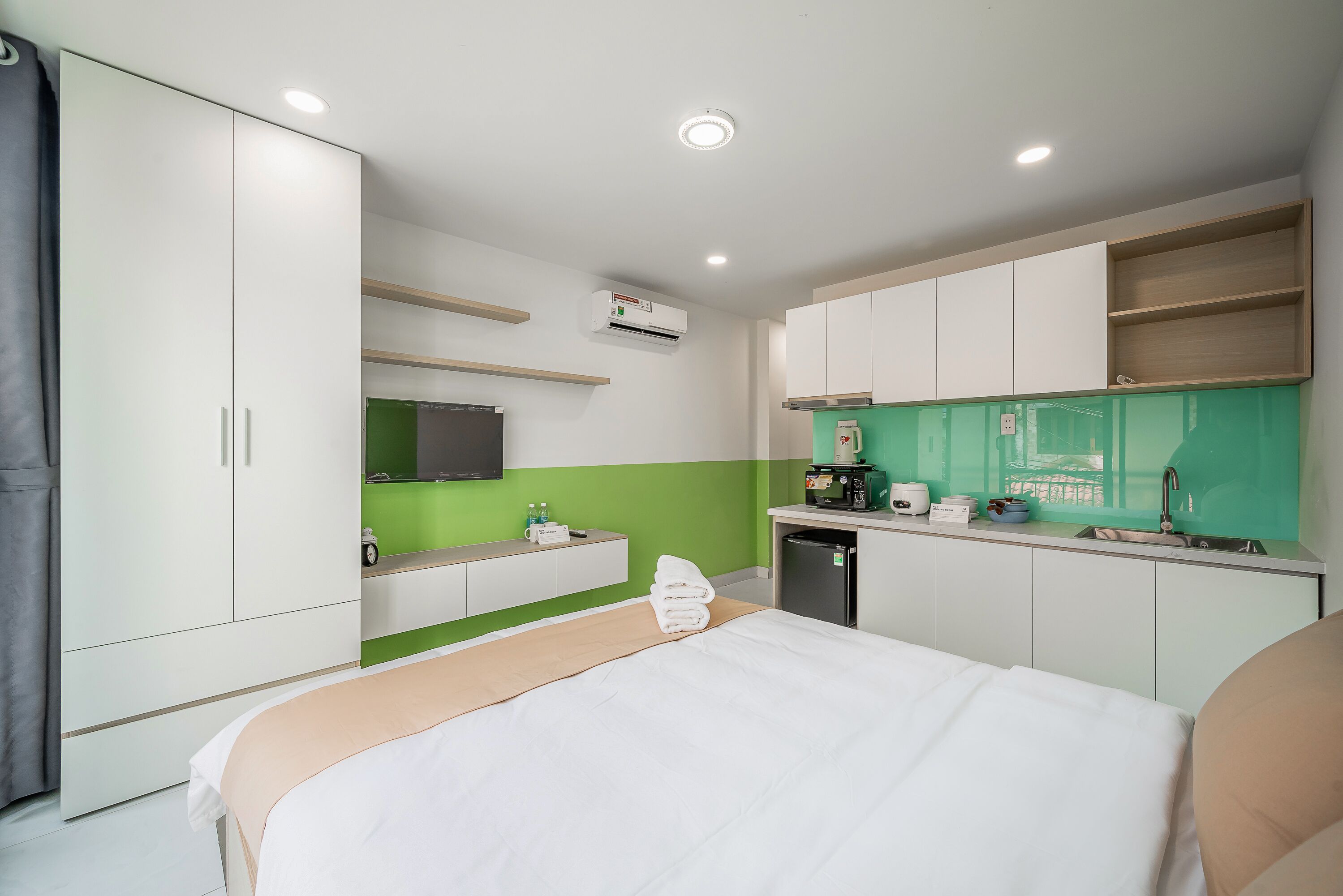 A hotel room with a bed, a kitchenette, a TV, and a green accent wall.