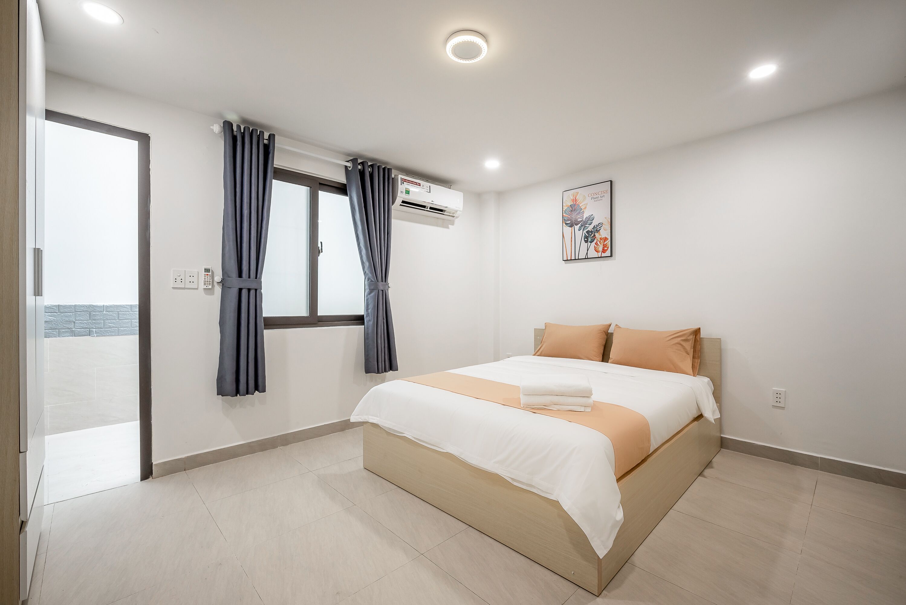 A modern bedroom with a large bed, a window with curtains, an air conditioning unit, and a wall-mounted artwork.