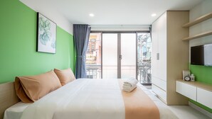 Hotellihuone, jossa on suuri sänky, vihreä seinä, taulu, televisio ja parveke, jolta on näkymä.