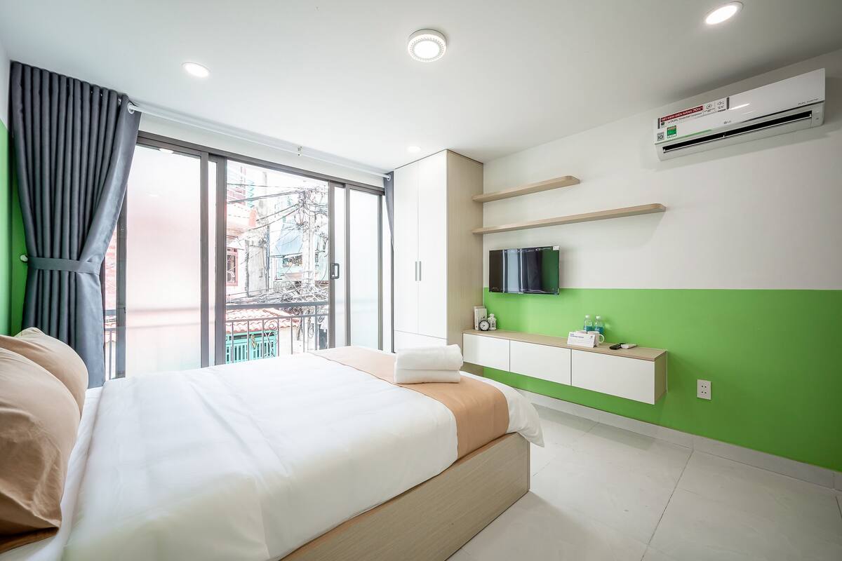 Ein modernes Hotelzimmer mit einem großen Bett, einer grünen Akzentwand, einem an der Wand befestigten Fernseher und einem Fenster mit Stadtblick.