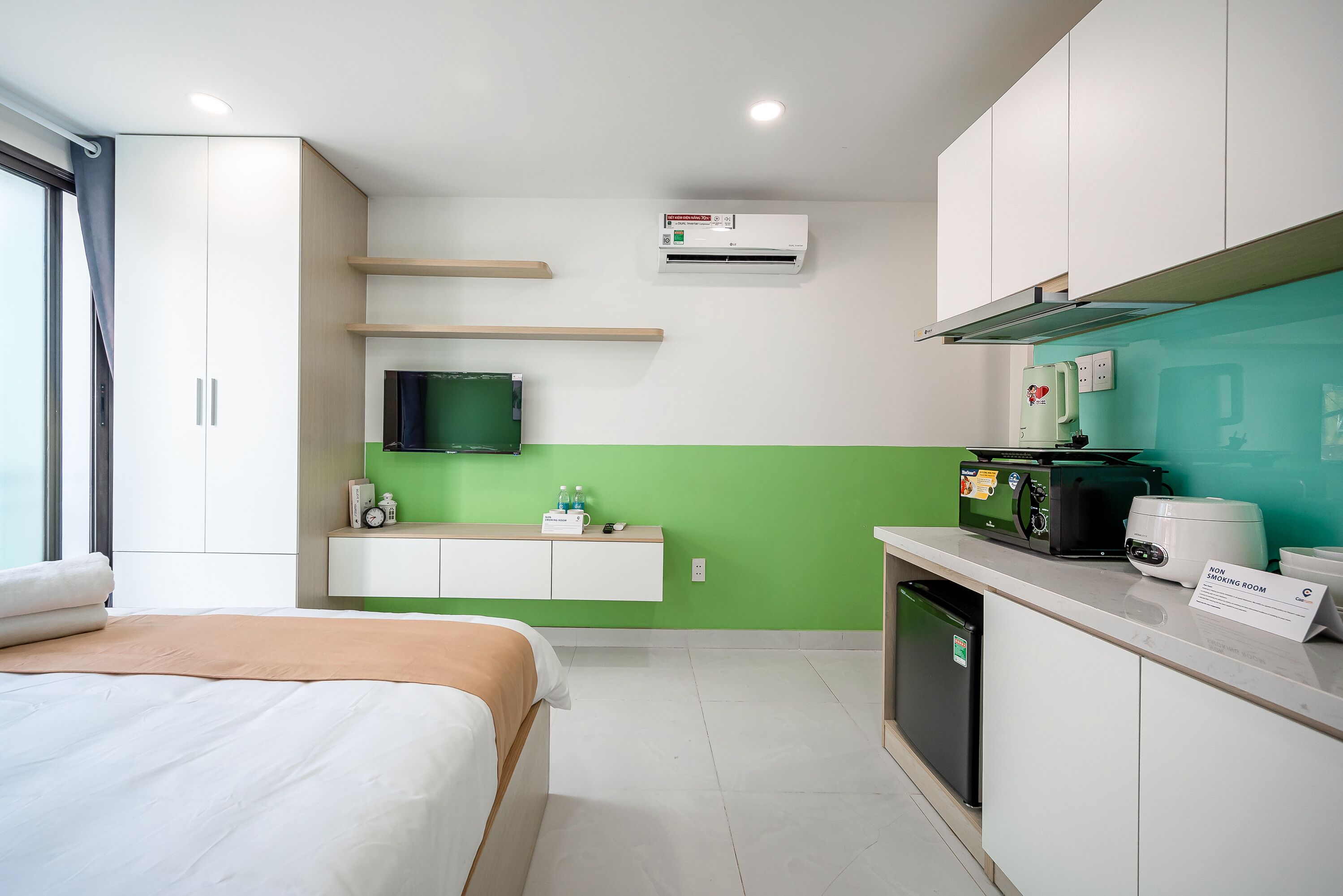 A hotel room with a bed, a kitchenette, a green accent wall, and a sign indicating it is a non-smoking room.