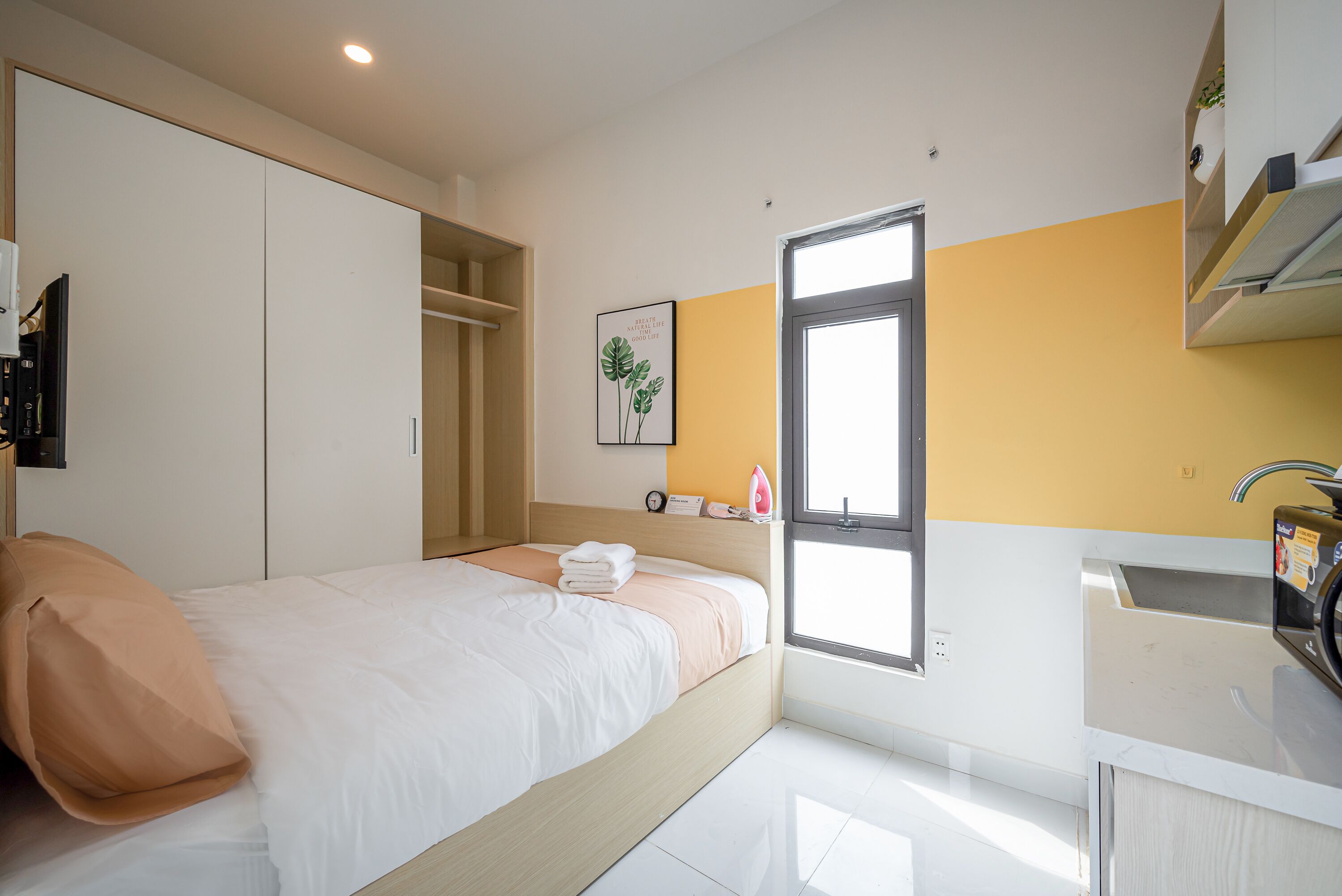 Un dormitorio con cama, armario, ventana y kitchenette.