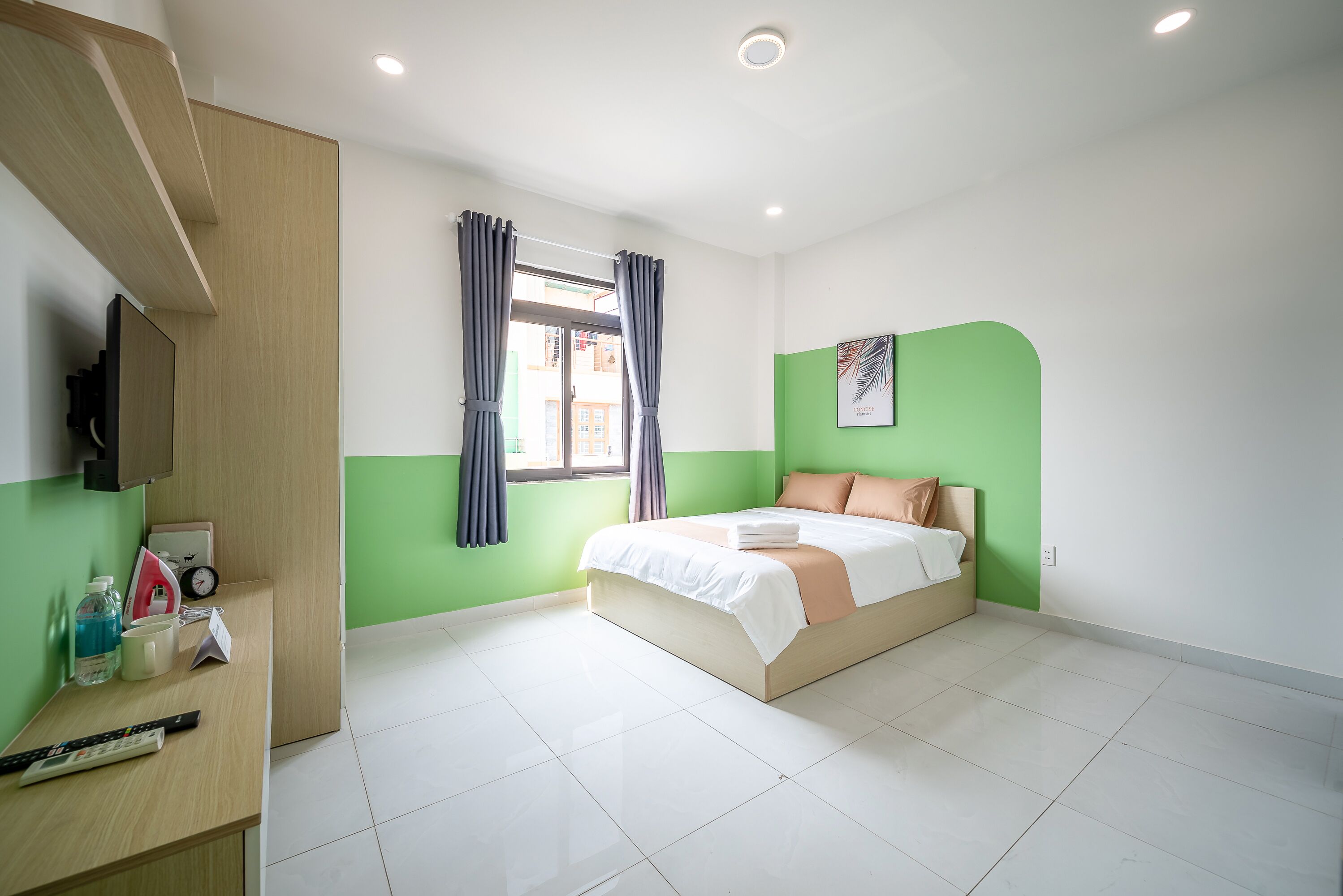 Un dormitorio con una cama, un escritorio con computadora, una ventana con cortinas y una pared verde decorativa.