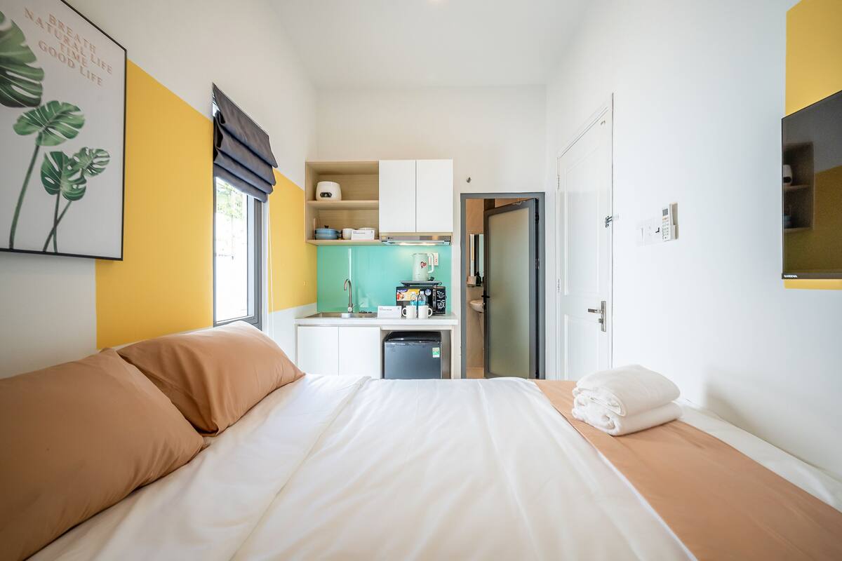 Ein kleines Hotelzimmer mit Bett, einer kleinen Küchenzeile und einem durch eine offene Tür einsehbarer Badezimmer.