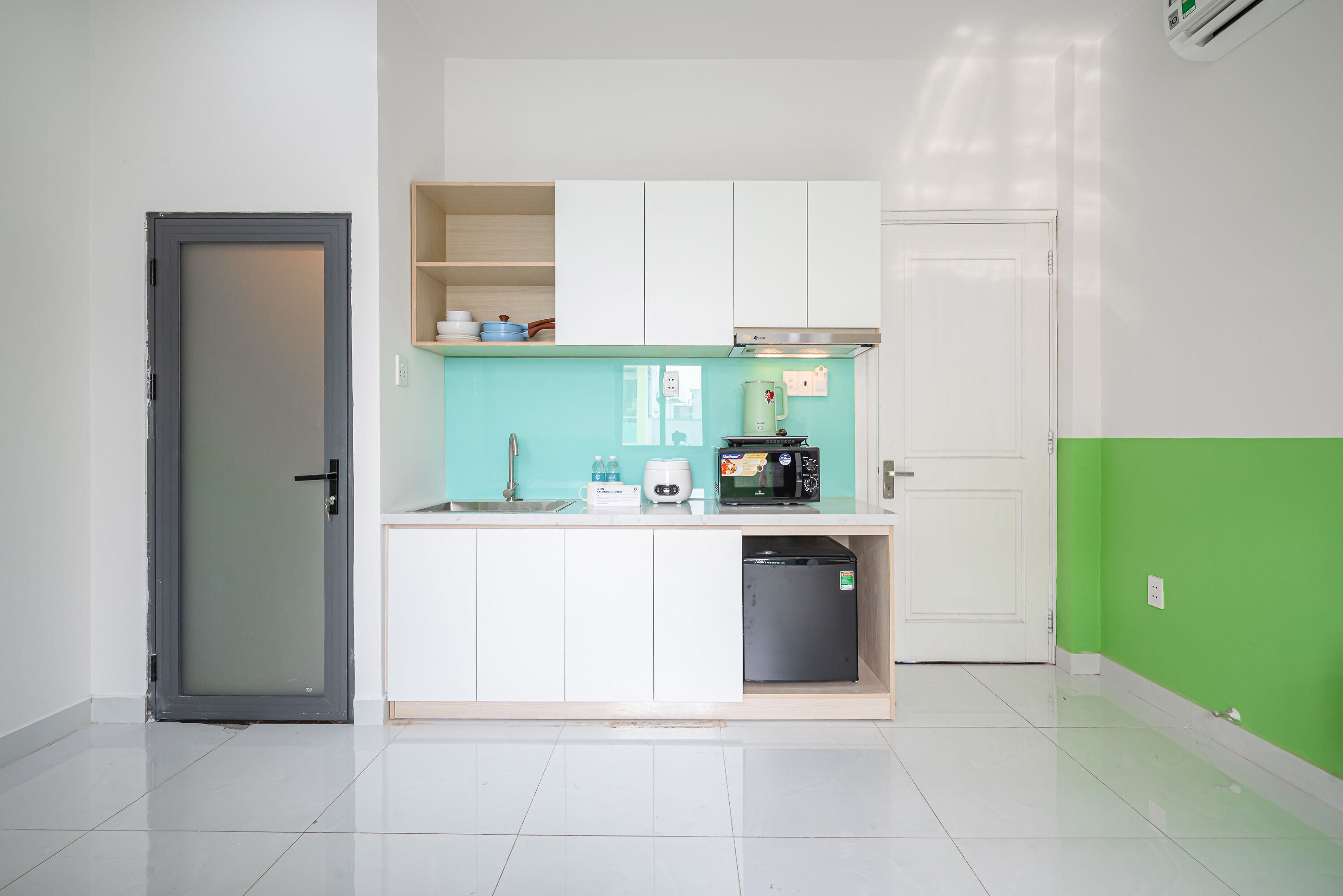 Una cocina compacta con armarios blancos, microondas, cafetera y un refrigerador pequeño.