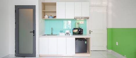 Una cocina compacta con armarios blancos, microondas, cafetera y un refrigerador pequeño.