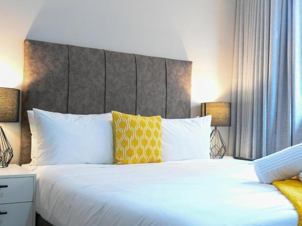 Habitación de hotel con una cama grande, dos lámparas de noche, una mesita de noche y una ventana con cortinas.
