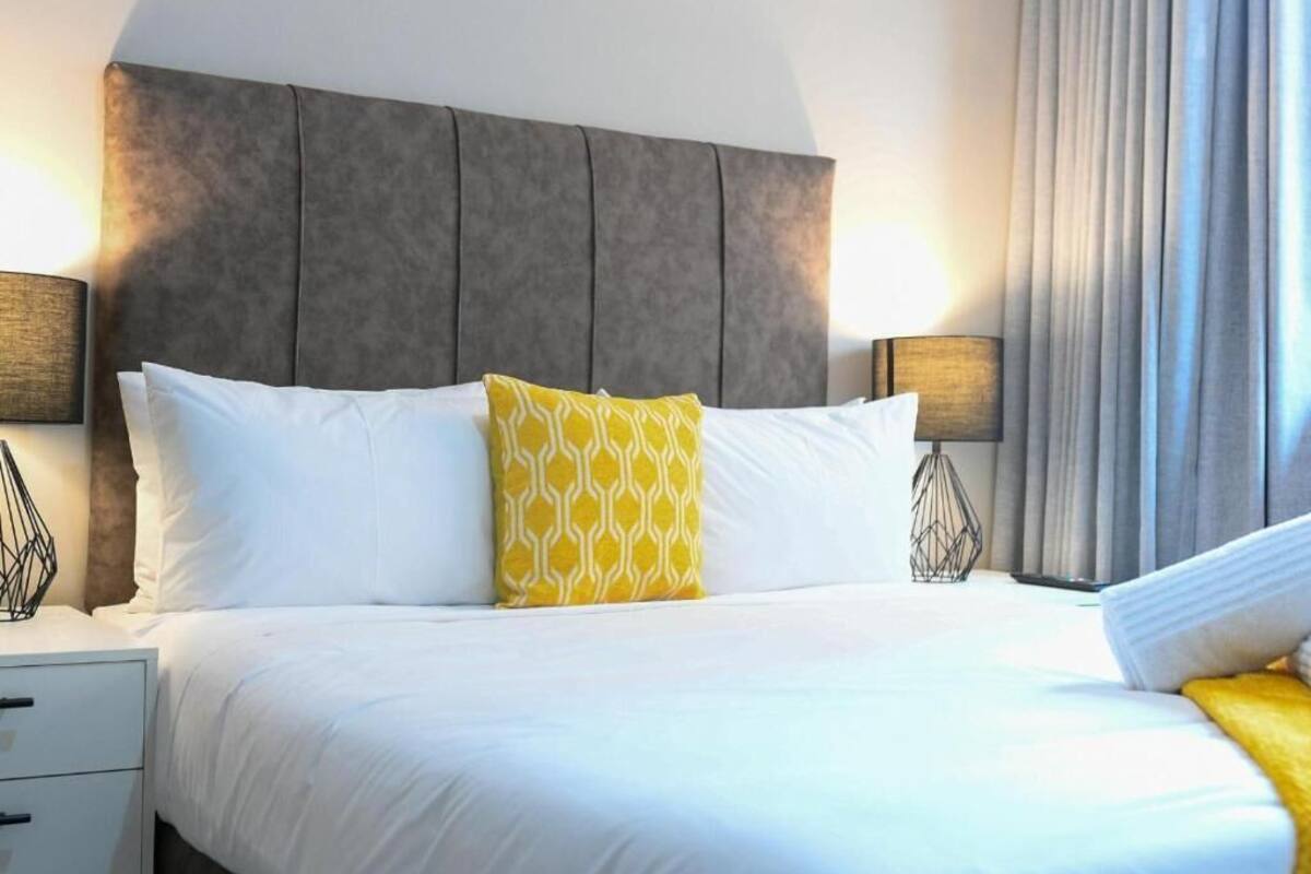 Habitación de hotel con una cama grande, dos lámparas de noche, una mesita de noche y una ventana con cortinas.