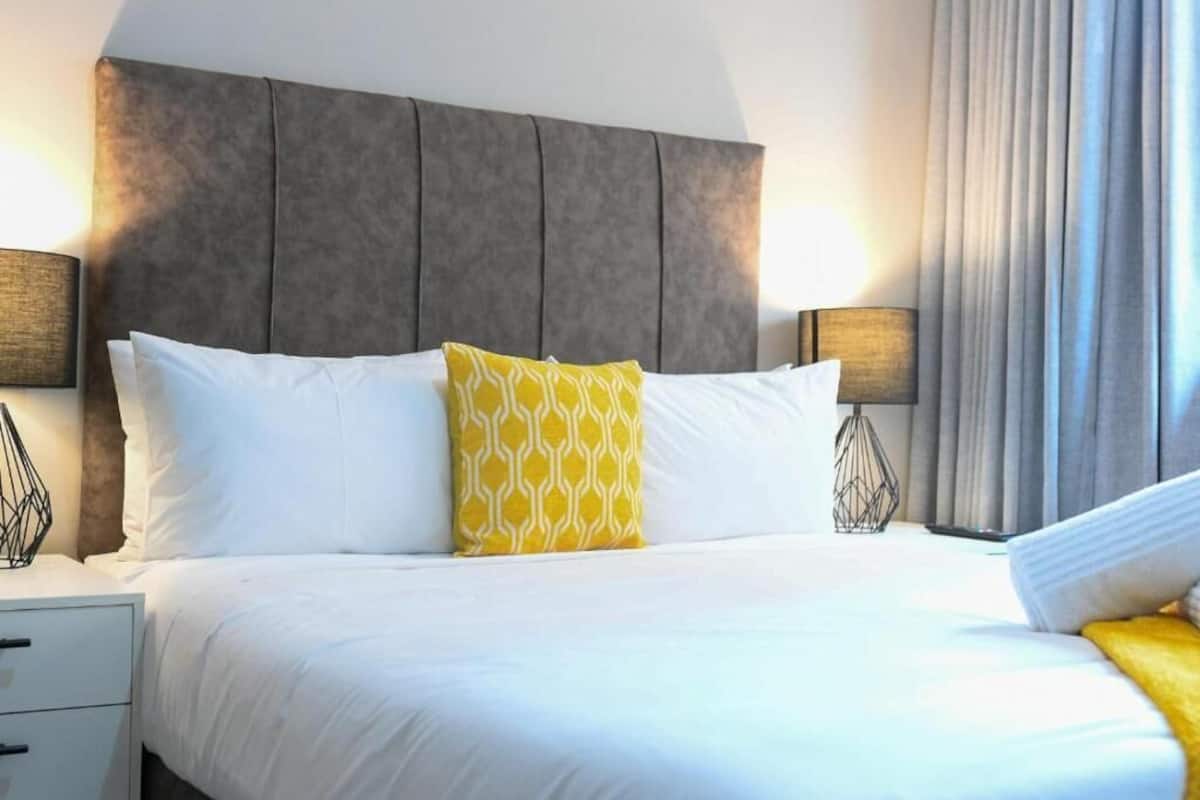 A hotel room with a large bed, two bedside lamps, a nightstand, and a window with curtains.