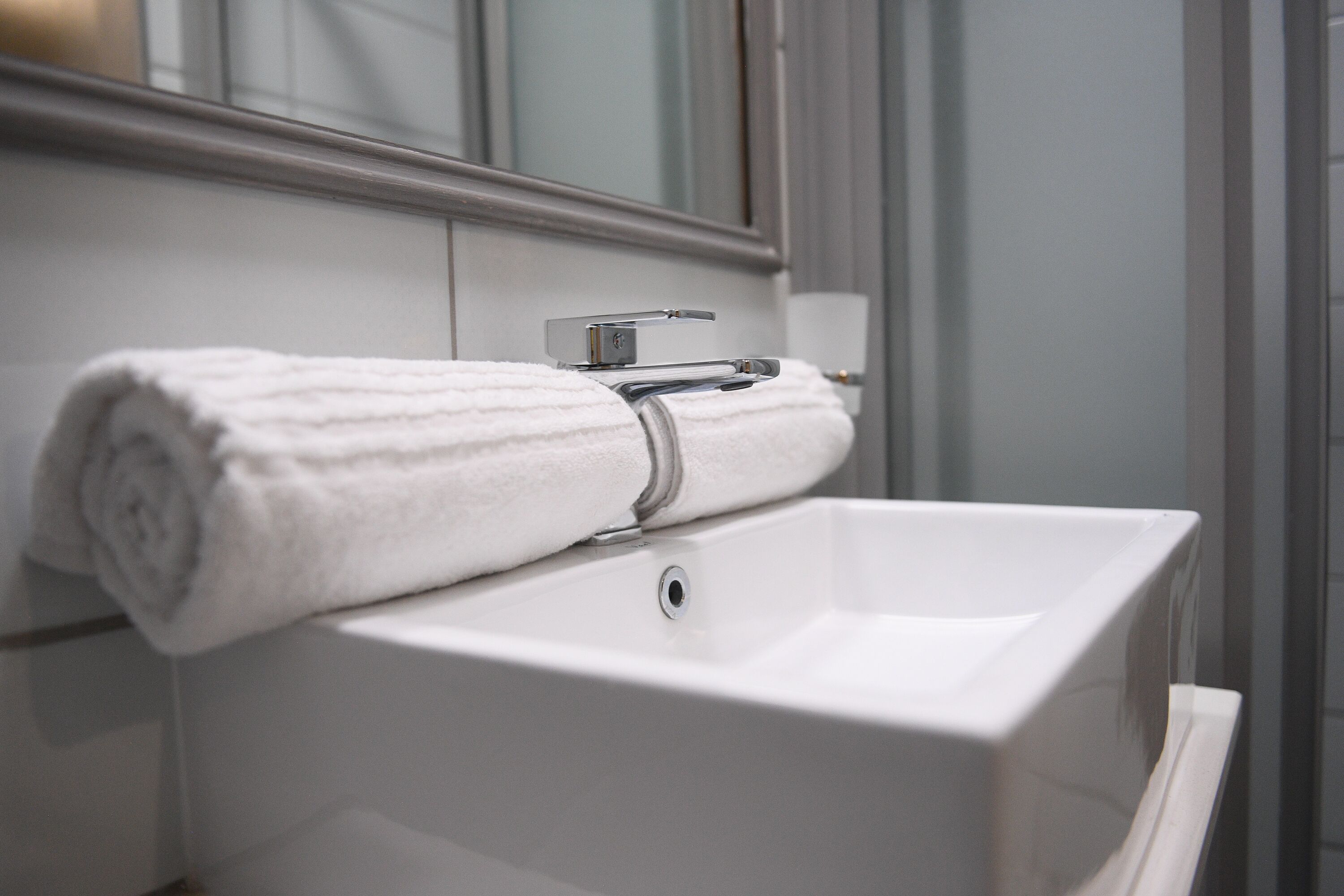 Un lavabo blanc dans une salle de bain, avec une serviette posée dessus et un miroir au-dessus.