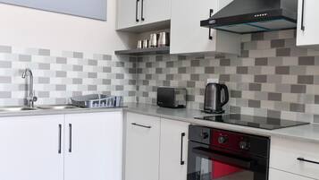 Een moderne keuken met witte kasten, een roestvrijstalen spoelbak, een broodrooster, een waterkoker en een rode oven.