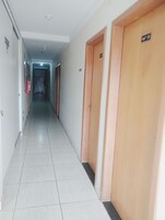 Corredor comprido e estreito, com piso de azulejos e portas de madeira à direita.
