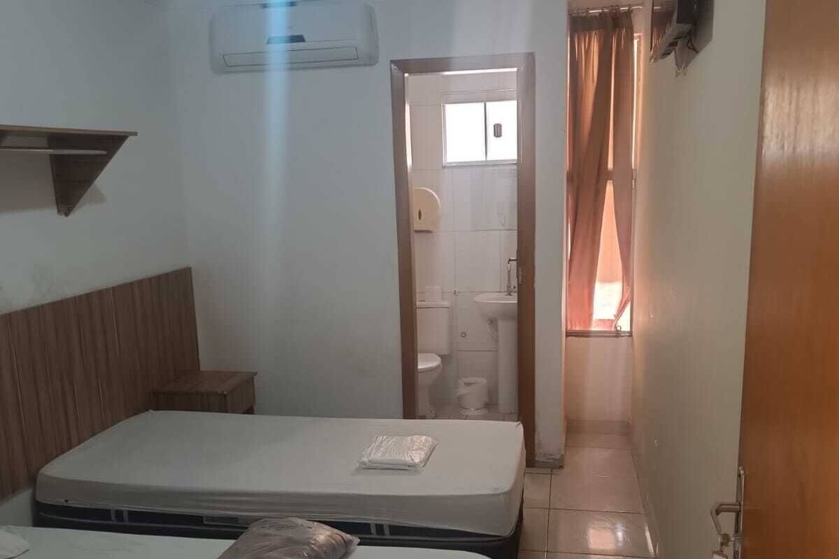 Une chambre d’hôtel avec deux lits, une tête de lit en bois, une petite table, un téléviseur fixé au mur et une salle de bain visible à travers une porte ouverte.