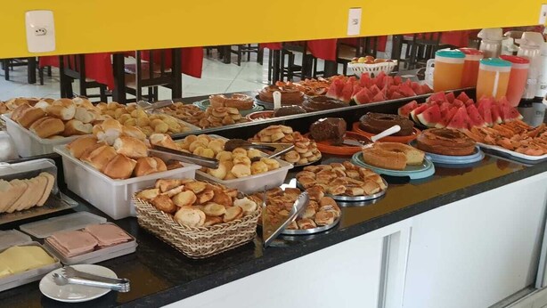 Buffet com diversos alimentos, incluindo pão, doces e frutas.