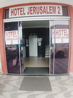 A entrada do Hotel Jerusalem 2, com uma placa visível, piso de azulejos e uma porta que dá acesso ao interior.