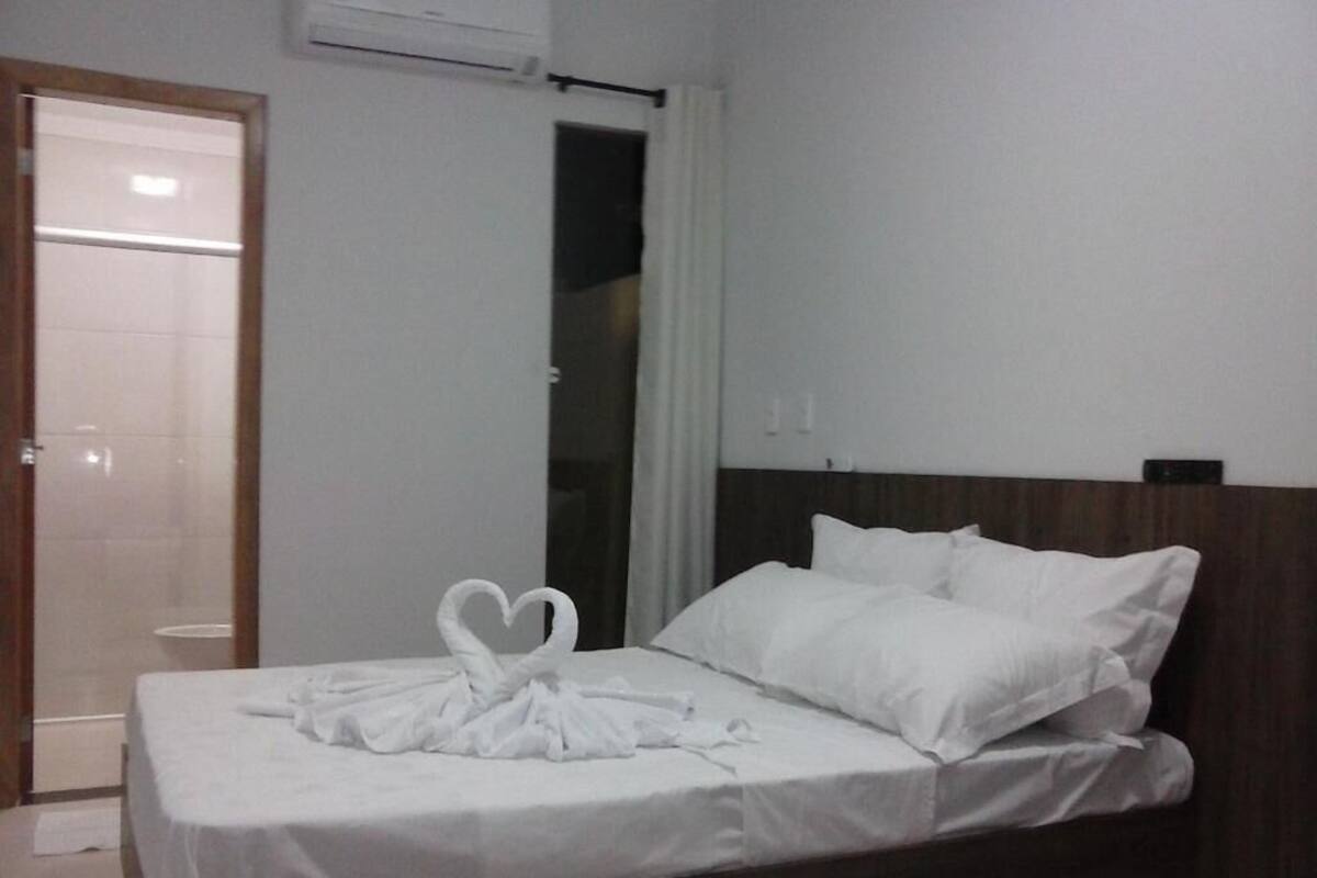 Une chambre d’hôtel avec un lit, du linge de lit blanc, une tête de lit en bois et une serviette joliment disposée sur le lit.