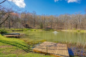 A serene lakeside setting with a wooden dock, a bench, and a small building in the background.