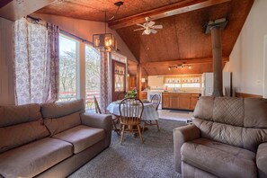 A cozy living room with a high ceiling, a dining area with wooden chairs, and a kitchen visible through an open door.