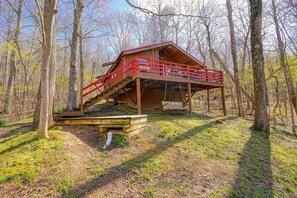 A wooden cabin with a red railing and a swing chair in a forest.