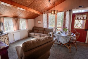 Una habitación acogedora con techo de madera, un sofá de cuero marrón, una mesa de comedor con sillas y una puerta roja.