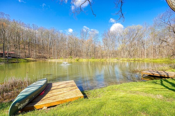 A serene lakeside setting with a wooden dock and a canoe, surrounded by trees and a clear sky.