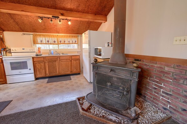 A kitchen with a wood-burning stove, a refrigerator, and wooden cabinets.