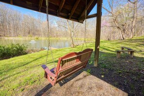A wooden swing set with a bench, a picnic table, and a pond in a park.