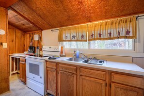 A kitchen with wooden cabinets, a stove, a sink, and a window with star-patterned curtains.
