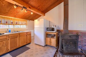 Eine Küche mit Holzschränken, einem weißen Kühlschrank, einer Mikrowelle und einem Kaminofen.