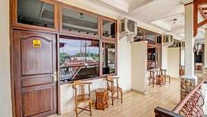 A room with a wooden door marked '323', a balcony with a view of buildings, and a seating area with chairs and a small table. - Collection O 92242 Hotel Tanjung Emas (Purwokerto)
