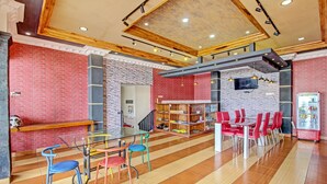 A spacious indoor area with a high ceiling, red brick walls, and a mix of wooden and metal furniture. - Collection O 92242 Hotel Tanjung Emas (Purwokerto)