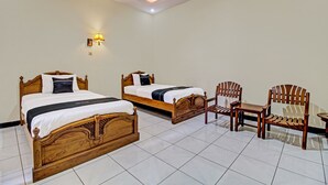 A hotel room with two wooden beds, a small wooden table, and a chair. - Collection O 92242 Hotel Tanjung Emas (Purwokerto)