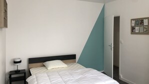 A bedroom with a bed, a nightstand, a wall-mounted light, and a door.