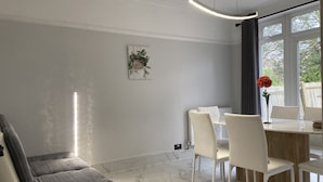 Een moderne woonkamer met een grijze bank, een eettafel met witte stoelen, een marmeren vloer en een raam met gordijnen.