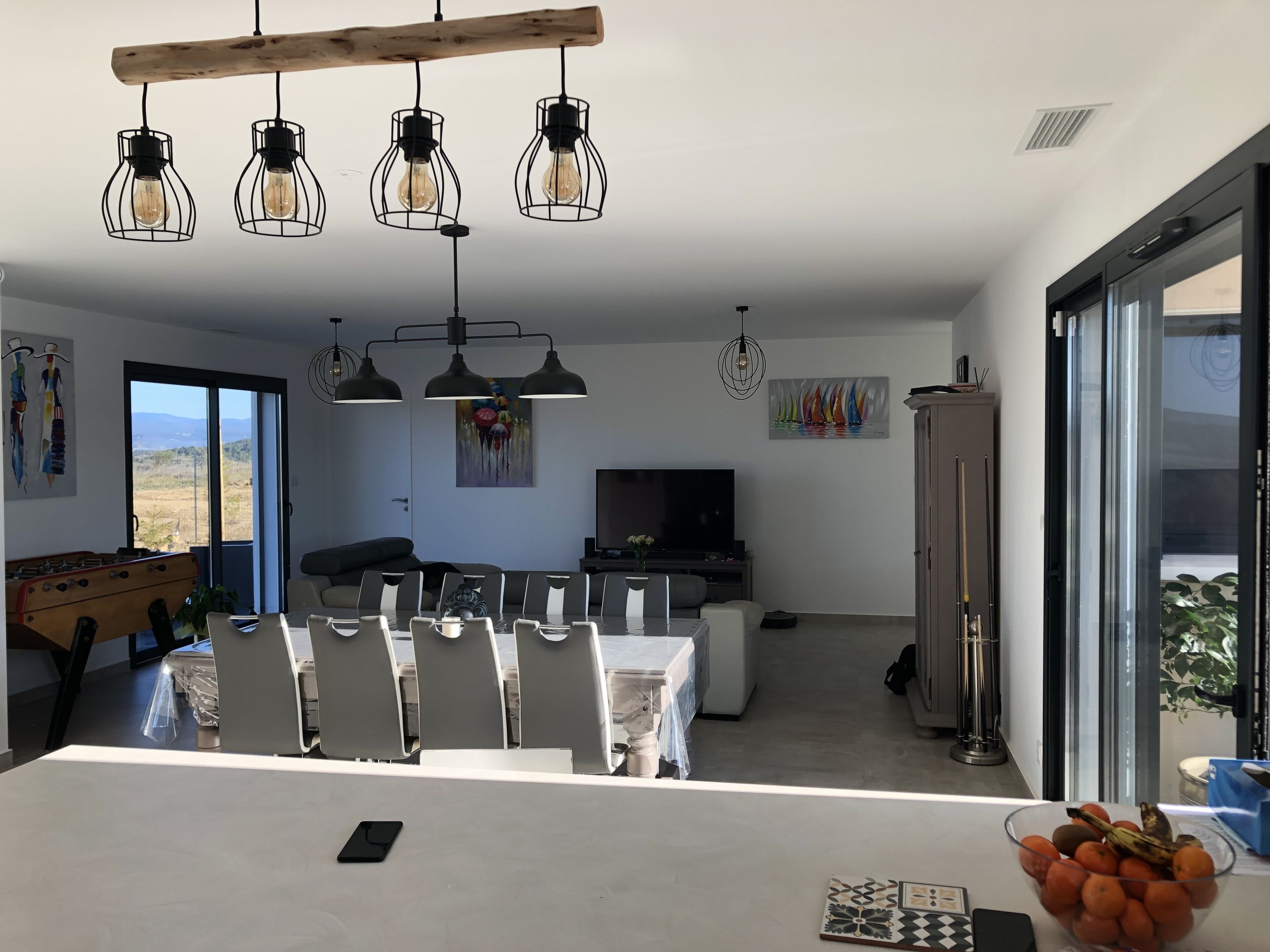 Un espace de salle à manger moderne, doté d’une grande table, de chaises et de luminaires suspendus.