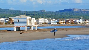 Una playa con una fila de casas, una torre de salvavidas y una persona cargando una tabla de surf.