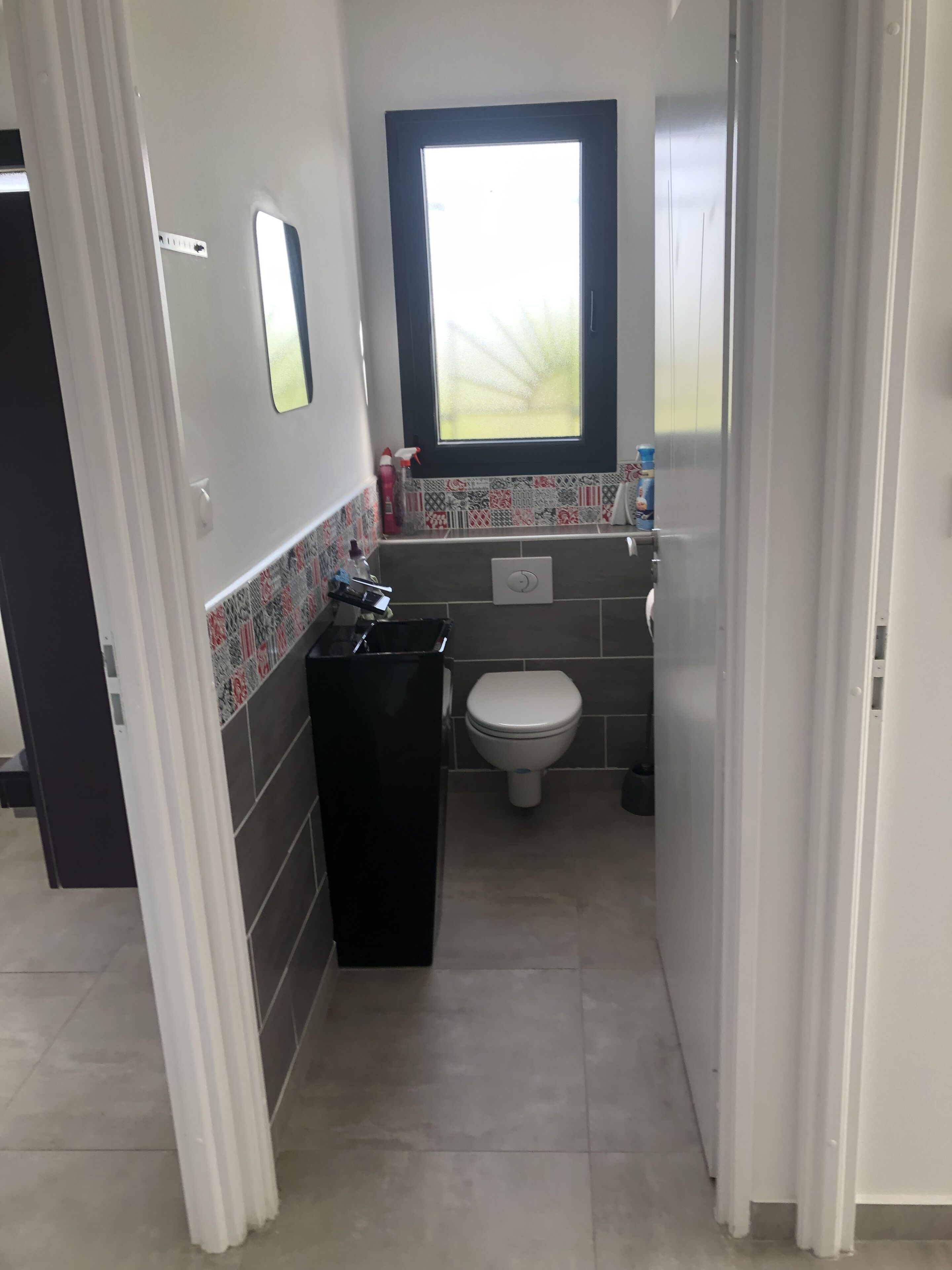 A compact bathroom with a toilet, a window, and a tiled backsplash.