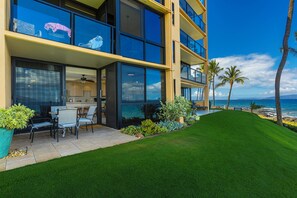 Un edificio moderno con grandes ventanales, un patio con mobiliario exterior y vista al océano.