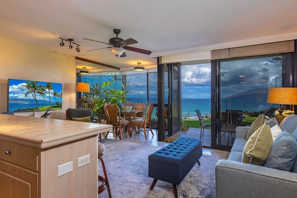 Una sala de estar moderna con un amplio ventanal con vistas al océano, un comedor con panorama y una cocina con barra.