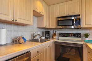 Una cocina con armarios de madera, un microondas de acero inoxidable, una estufa y un fregadero.