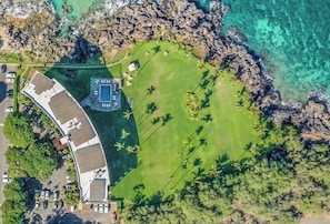 Vista aérea de una propiedad costera con piscina, zona de estacionamiento y área verde con palmeras.