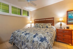 Un dormitorio con cama, dos mesitas de noche con lámparas, ventilador de techo y ventana con persianas.