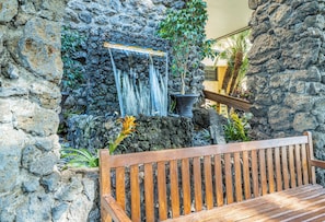 Un muro de piedra con una cascada y un banco de madera.