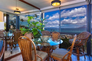 A dining area with wicker chairs and a glass table, overlooking a scenic ocean view.