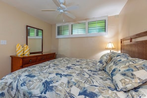 Un dormitorio con cama, ventilador de techo, cómoda, espejo y ventana con persianas.
