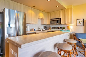 Una cocina moderna con armarios blancos, electrodomésticos de acero inoxidable y una isla central con taburetes de bar.